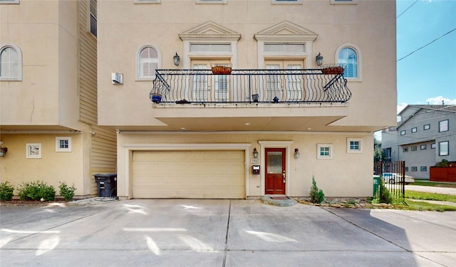 view of property with a garage, concrete driveway, a balcony, and stucco siding