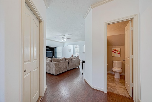 corridor with baseboards, arched walkways, dark wood-type flooring, crown molding, and a textured ceiling