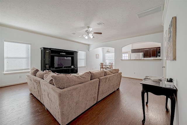 living area with arched walkways, dark wood-style floors, visible vents, and baseboards