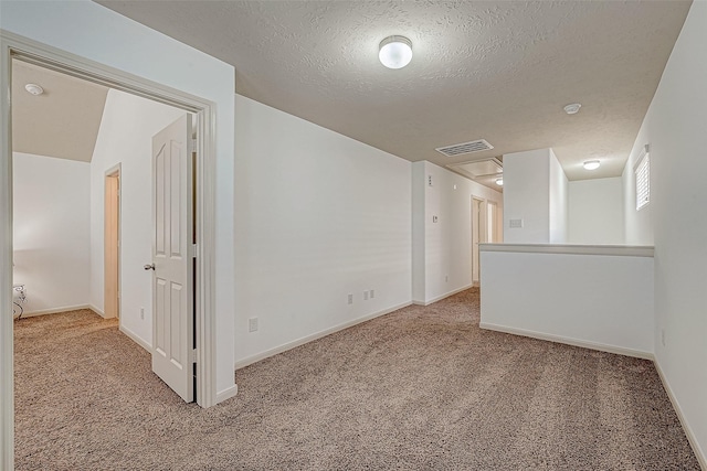 carpeted spare room featuring a textured ceiling, visible vents, and baseboards