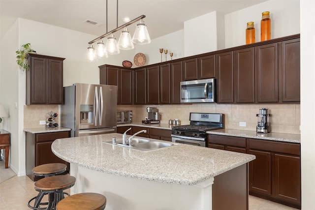 kitchen featuring dark brown cabinetry, a sink, a kitchen breakfast bar, appliances with stainless steel finishes, and a center island with sink