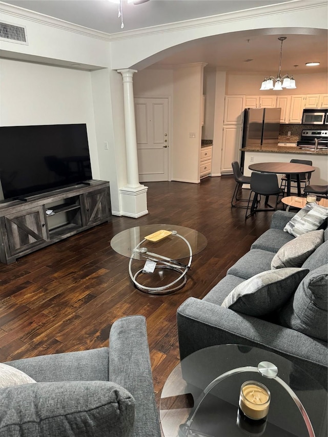 living room with arched walkways, dark wood-type flooring, visible vents, and ornate columns