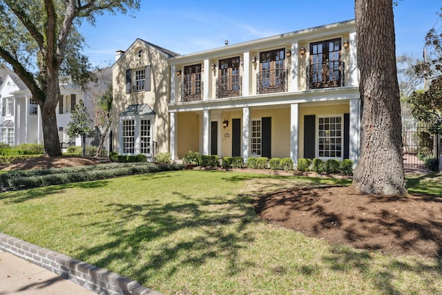 view of front facade with a balcony, fence, covered porch, a front lawn, and french doors