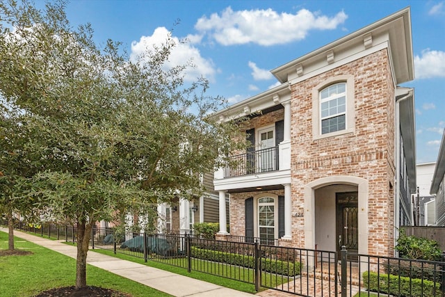 italianate house with brick siding, a fenced front yard, a front yard, and a balcony