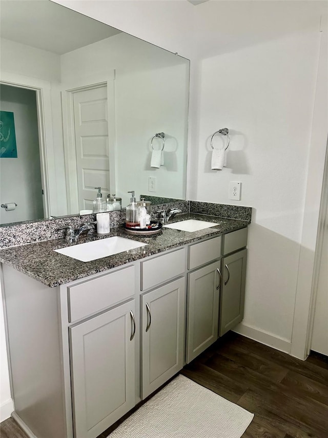 full bathroom with double vanity, baseboards, a sink, and wood finished floors