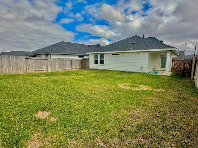 rear view of property featuring roof with shingles, a lawn, and a fenced backyard