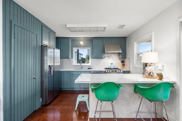 kitchen with stainless steel fridge, visible vents, a peninsula, wall chimney range hood, and a sink