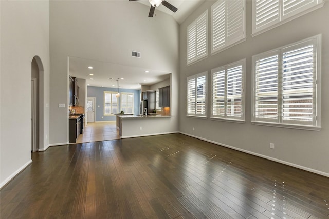 unfurnished living room with ceiling fan, visible vents, arched walkways, and dark wood-style flooring