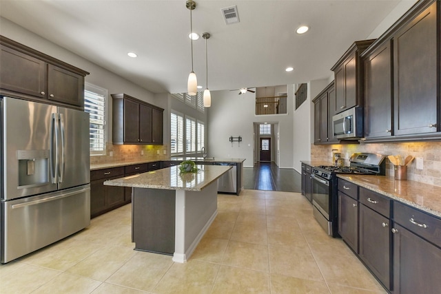 kitchen with pendant lighting, stainless steel appliances, a kitchen island, dark brown cabinets, and light stone countertops