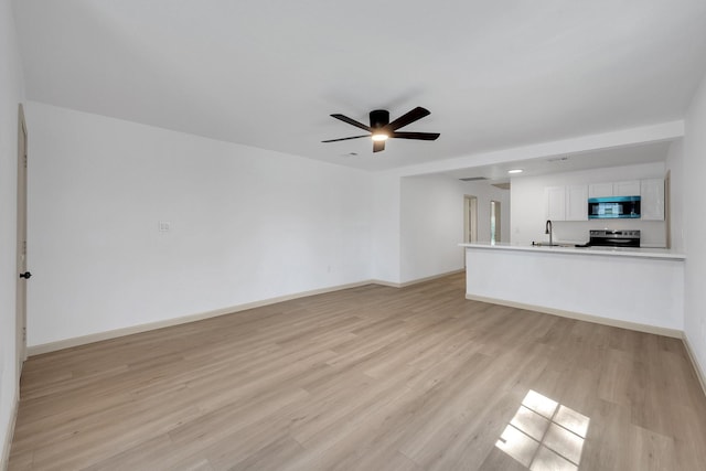 unfurnished living room with a ceiling fan, light wood-type flooring, a sink, and baseboards