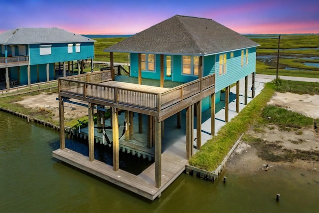 back of house at dusk featuring a shingled roof, a water view, driveway, and a carport