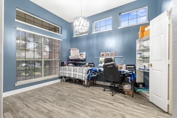 office space featuring light wood-type flooring, an inviting chandelier, a high ceiling, and baseboards