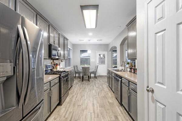 kitchen with light wood-style flooring, hanging light fixtures, stainless steel appliances, light countertops, and a sink