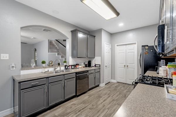 kitchen featuring arched walkways, stainless steel appliances, light countertops, gray cabinetry, and a sink