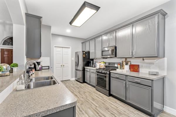 kitchen with light countertops, appliances with stainless steel finishes, gray cabinets, and a sink