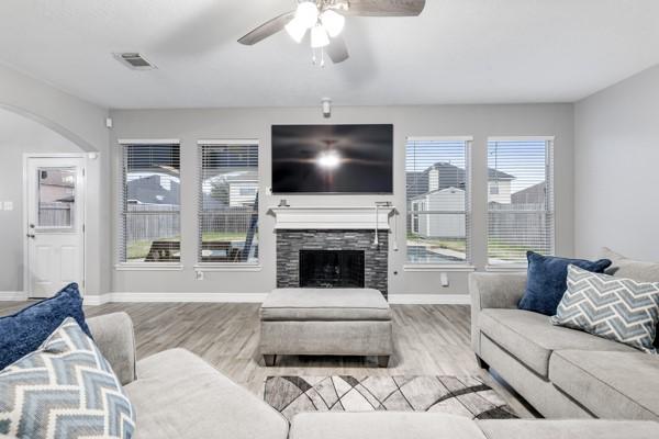 living room with baseboards, visible vents, a stone fireplace, and light wood finished floors