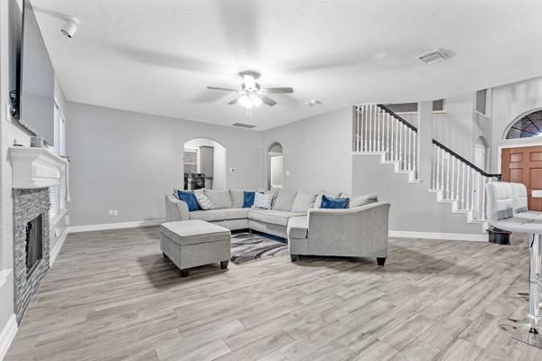 living room with arched walkways, a stone fireplace, light wood-type flooring, baseboards, and stairs