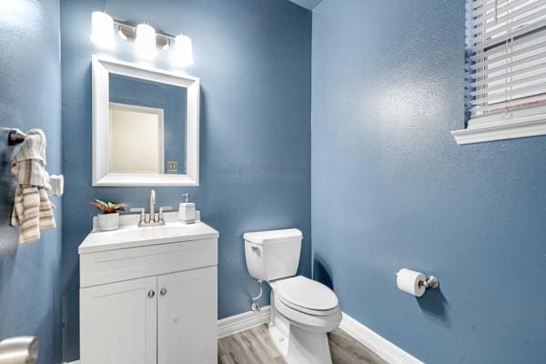 half bath featuring baseboards, vanity, toilet, and wood finished floors