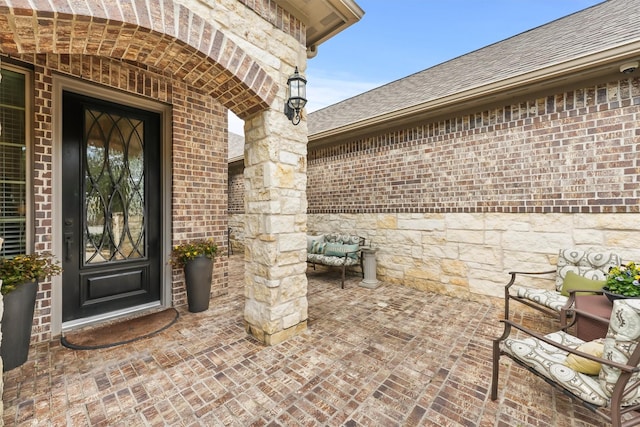 entrance to property featuring a shingled roof and brick siding