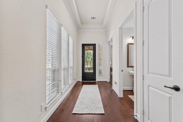 foyer featuring dark wood-style flooring, visible vents, baseboards, ornamental molding, and a tray ceiling