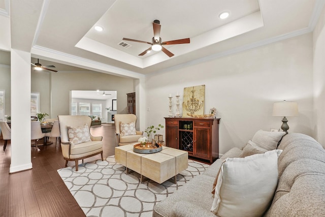 living area with light wood finished floors, visible vents, a raised ceiling, ceiling fan, and crown molding