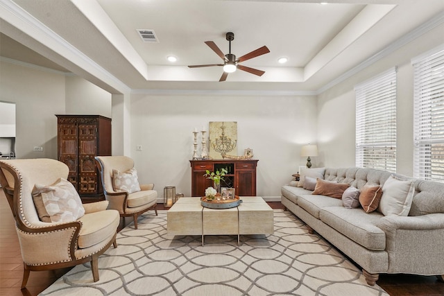 living room with visible vents, baseboards, a ceiling fan, ornamental molding, and a raised ceiling