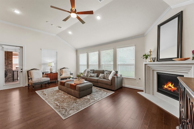 living area with baseboards, a glass covered fireplace, ornamental molding, dark wood-style flooring, and vaulted ceiling