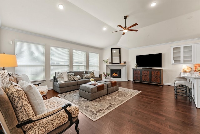 living area featuring dark wood-style flooring, ornamental molding, a glass covered fireplace, vaulted ceiling, and ceiling fan