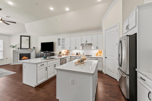 kitchen featuring stainless steel appliances, glass insert cabinets, open floor plan, a kitchen island, and a sink