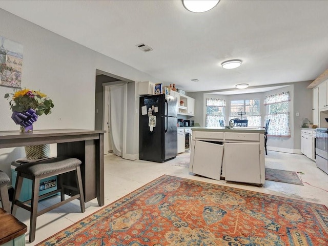 kitchen featuring light countertops, freestanding refrigerator, white cabinetry, and visible vents