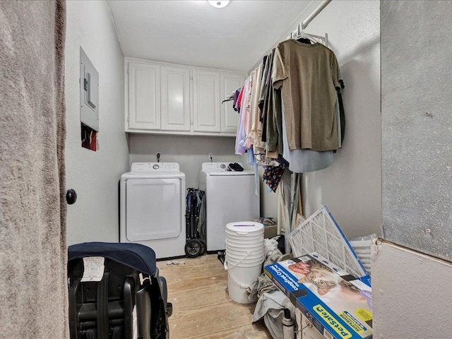 clothes washing area featuring light wood-style floors, electric panel, cabinet space, and washing machine and clothes dryer