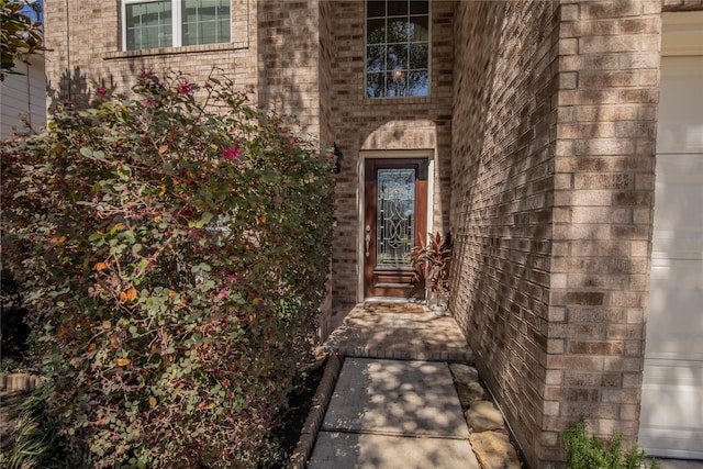 view of exterior entry featuring a garage and brick siding