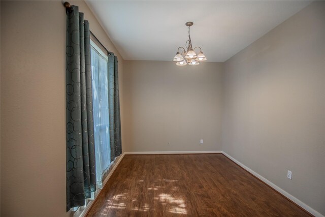 empty room featuring a chandelier, baseboards, and wood finished floors