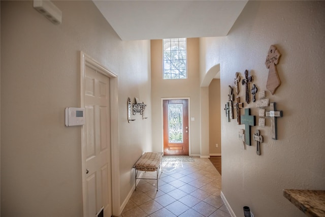 foyer with arched walkways, a towering ceiling, baseboards, and light tile patterned flooring