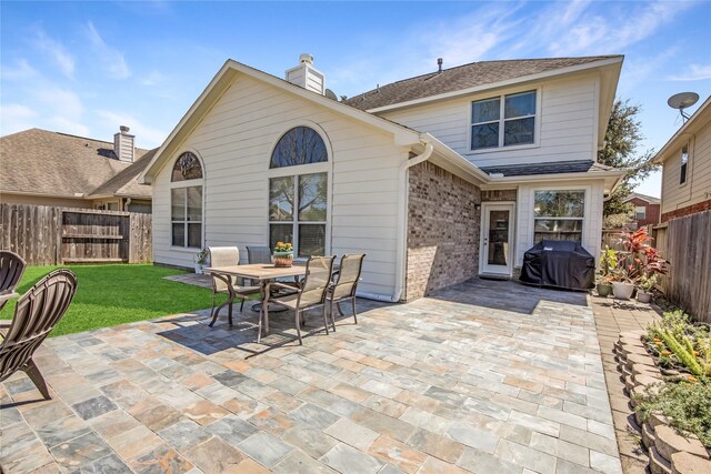 back of house with brick siding, a shingled roof, a lawn, a fenced backyard, and a patio area