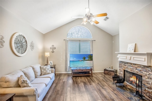 living room featuring visible vents, baseboards, vaulted ceiling, a stone fireplace, and wood finished floors