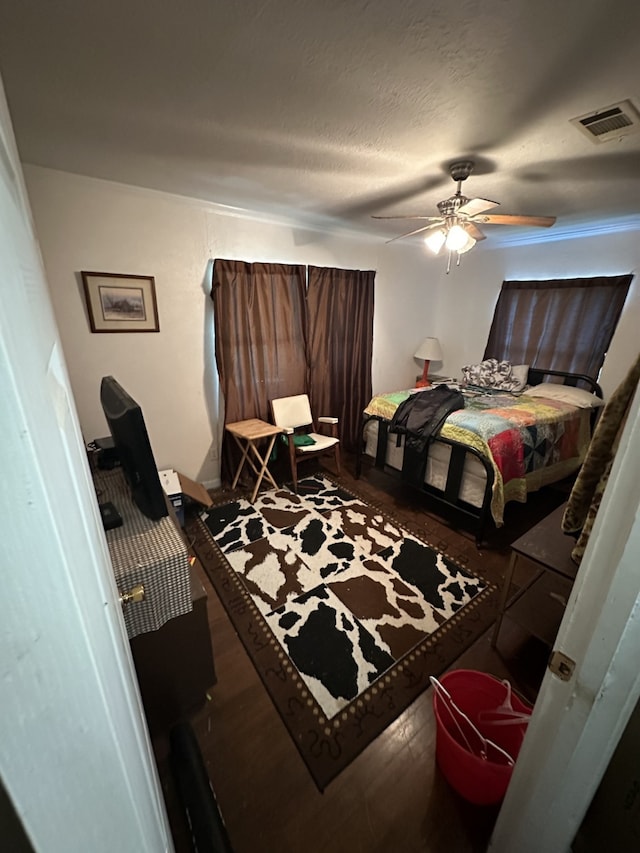 bedroom with a textured ceiling, wood finished floors, visible vents, and a ceiling fan