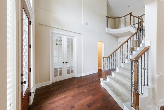 foyer featuring french doors, dark wood-style flooring, visible vents, a towering ceiling, and baseboards