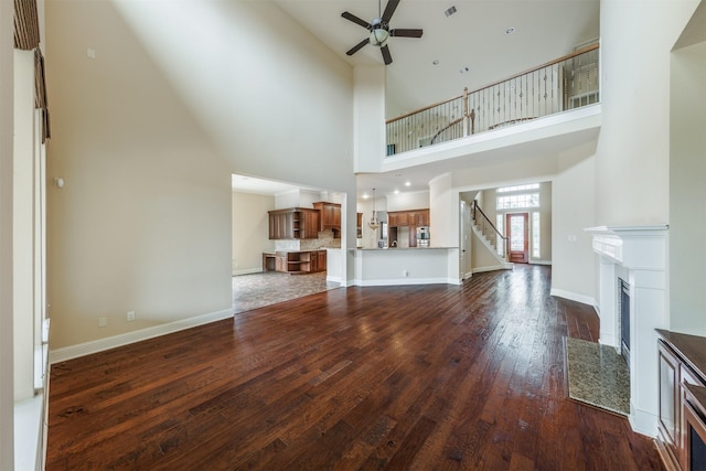 27711 Rocky Creek Ct, Fulshear, TX 77441 - unfurnished living room featuring ceiling fan, stairway, a high ceiling, a fireplace with flush hearth, and dark wood-type flooring