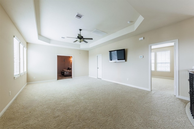 spare room with light colored carpet, a tray ceiling, visible vents, and baseboards