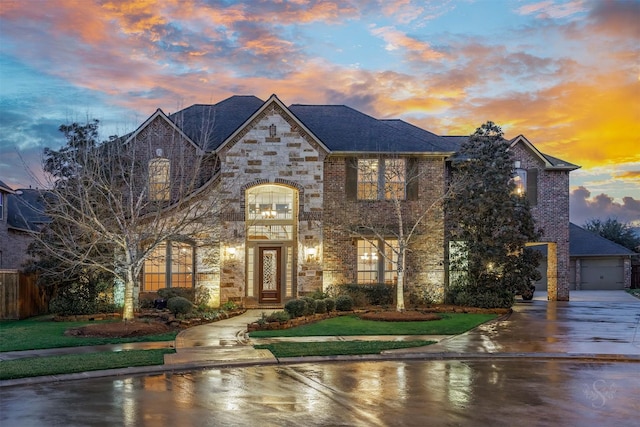 french provincial home with a garage, stone siding, brick siding, and fence