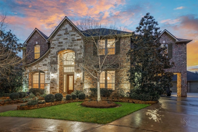 french country inspired facade with stone siding, brick siding, and a lawn