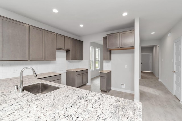 kitchen with light stone counters, a sink, backsplash, and light wood finished floors