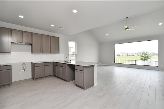 kitchen with a peninsula, a sink, visible vents, light wood-type flooring, and backsplash