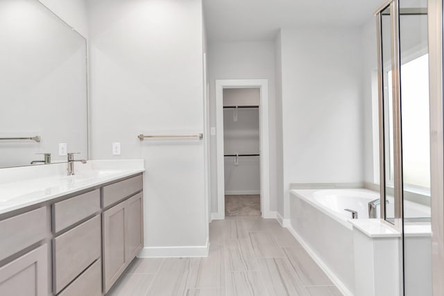 bathroom featuring a walk in closet, a garden tub, a wealth of natural light, vanity, and baseboards