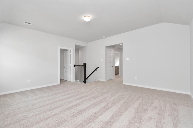 unfurnished room featuring light colored carpet, visible vents, vaulted ceiling, and baseboards