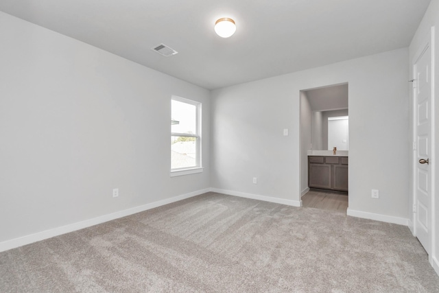 unfurnished bedroom with light carpet, ensuite bathroom, visible vents, and baseboards