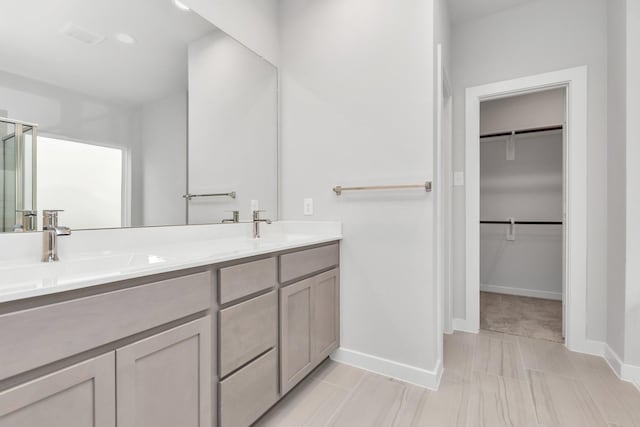 full bath with a spacious closet, double vanity, a sink, and baseboards