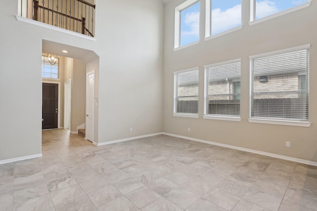 unfurnished room with a chandelier, a towering ceiling, and baseboards