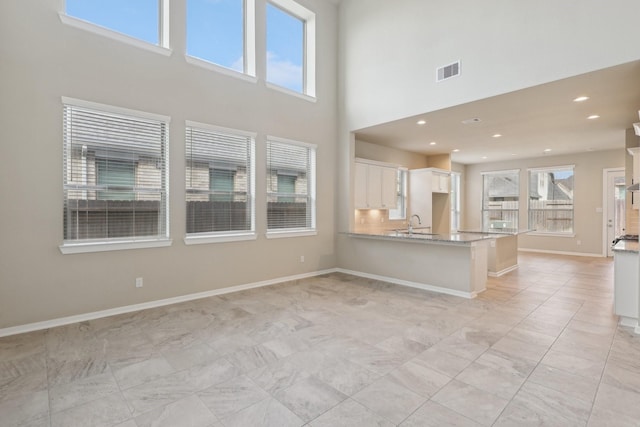 unfurnished living room featuring recessed lighting, a sink, a towering ceiling, visible vents, and baseboards